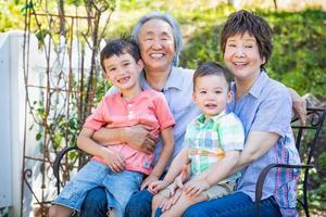los abuelos chinos y los niños de raza mixta se sientan en un banco al aire libre foto