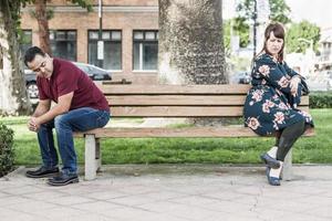 infeliz pareja de raza mixta sentados uno frente al otro en un banco del parque foto