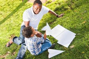 Happy African American Father and Mixed Race Son Playing with Paper Airplanes in the Park photo