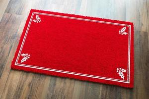 Blank Holiday Red Welcome Mat With Holly Corners On Wood Floor Background photo