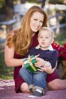 niño sosteniendo un regalo de navidad con su mamá en el parque foto