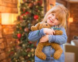 Girl Holding Teddy Bear In Front of Decorated Christmas Tree photo