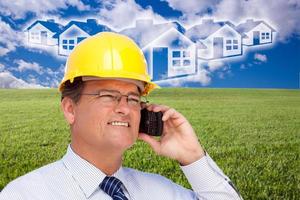 Contractor in Hardhat on Phone Over House, Grass and Clouds photo