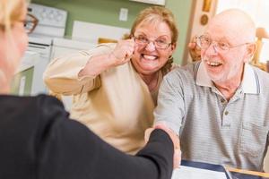 Senior Adult Couple Celebrating Over Documents in Their Home with Agent At Signing photo