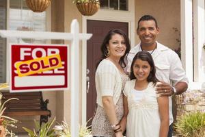familia hispana frente a su nuevo hogar con letrero vendido foto