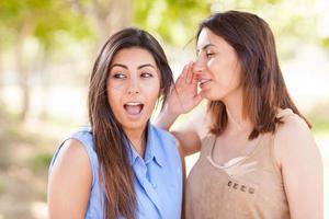 dos hermosas hermanas gemelas étnicas susurrando secretos al aire libre. foto