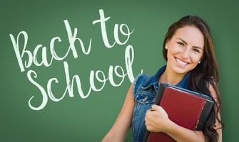 Back To School Written On Chalk Board Behind Mixed Race Young Girl Student Holding Books photo