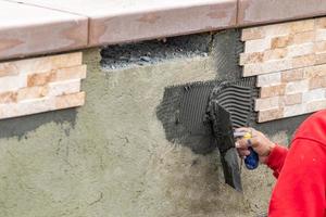 Worker Installing Wall Tile Cement with Trowel and Tile at Construction Site photo