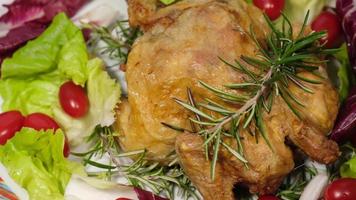 pollo al horno con ensalada y verduras de tomate girando en el plato. carne de ave a la parrilla con romero. video