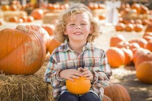 niño pequeño sentado y sosteniendo su calabaza en el huerto de calabazas foto