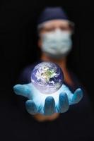 enfermera o médico con mascarilla y guantes quirúrgicos con palma bajo el planeta tierra flotante foto