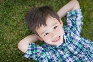 Mixed Race Chinese and Caucasian Young Boy Relaxing On His Back Outside On The Grass photo