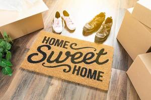 alfombra de bienvenida hogar dulce hogar, cajas de mudanza, zapatos de mujer y hombre y plantas en suelos de madera dura foto