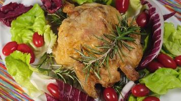 pollo al horno con ensalada y verduras de tomate girando en el plato. carne de ave a la parrilla con romero. video