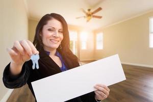 mujer hispana con llaves de casa y cartel en blanco en la habitación vacía de la casa foto