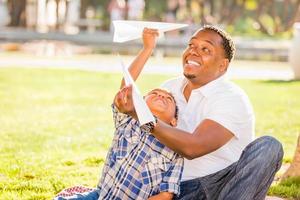 Happy African American Father and Mixed Race Son Playing with Paper Airplanes in the Park photo