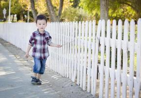 Joven muchacho de raza mixta caminando con bastón a lo largo de valla blanca foto