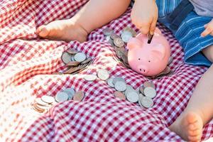 Baby Boy sentado en una manta para picnic poniendo monedas en la alcancía foto