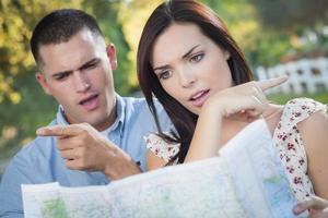 Lost and Confused Mixed Race Couple Looking Over Map Outside photo