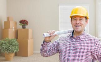 Male Construction Worker In Room With Boxes Holding Roll of Blueprints photo