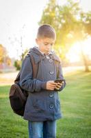 joven hispano caminando al aire libre con mochila enviando mensajes de texto por teléfono celular foto