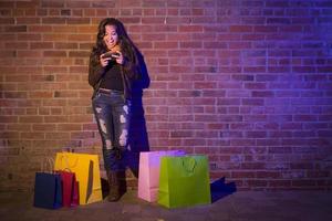 mujer con bolsas de compras usando un teléfono celular contra la pared de ladrillo foto
