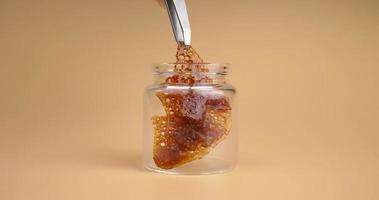 glass jar with brown cannabis wax, pieces of hardened resin of marijuana extract on an orange background video