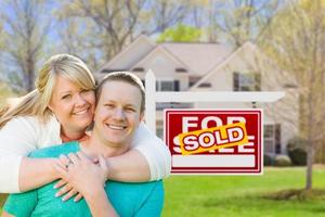 Happy Couple Hug In Front of Sold Real Estate Sign and New House photo