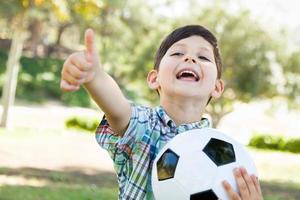 lindo joven jugando con balón de fútbol y pulgares arriba al aire libre en el parque. foto