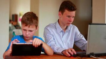 dos hermanos usando laptop y tablet en la mesa en casa