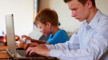 dois irmãos usando laptop e tablet à mesa em casa video