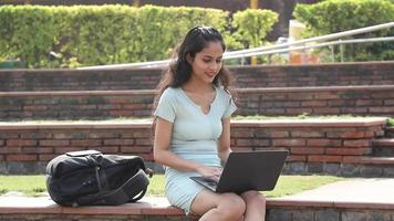 Videoclip de archivo de una estudiante que trabaja en su computadora portátil mientras está sentada en el campus. video