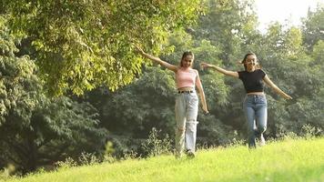 material de archivo de dos amigas alegres extendiendo sus brazos en el aire y corriendo en un parque. video