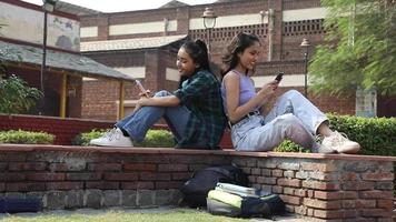 Stock video of an Indian college student enjoying chatting on their mobile phone while sitting on the university campus.