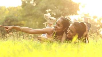 Video of two beautiful Indian girls lying on green grass and having fun in a park.