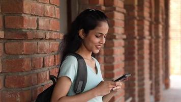 video clip di un' lato Visualizza di un' femmina Università alunno digitando testo su sua mobile Telefono su il Università città universitaria.