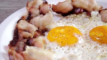 ovos de bacon frito e pimenta em um prato, grelhados e prontos para o café da manhã inglês. mesa de madeira. tiro deslizante. video