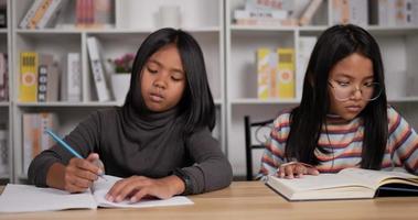 Porträt von zwei asiatischen Studentinnen, die am Schreibtisch im Klassenzimmer sitzen. mädchen brille lesebuch für prüfung und mädchen kurze haare machen hausaufgaben. Bildungskonzept. video