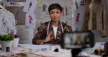 Portrait of Asian fashion designer or stylist live streaming on social about new clothes collection via smartphone in the studio. Woman tailor dressmakers prepares wardrobe clothing for sale. video