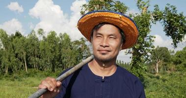 ralenti, portrait de l'agriculteur d'âge moyen portant une chemise et un chapeau de paille transportant du matériel et marchant dans les rizières video