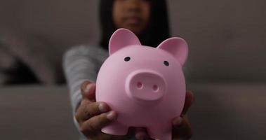 Closeup of piggy bank. Asian girl holds out a pink piggy bank. Young female with piggy bank. Financial, saving money and investment concept. video