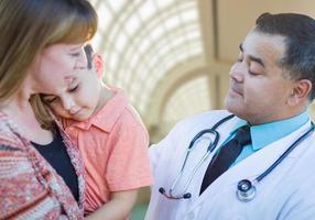 niño de raza mixta enfermo, madre y médico hispano dentro del hospital foto