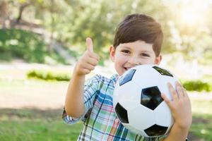 lindo joven jugando con balón de fútbol y pulgares arriba al aire libre en el parque. foto