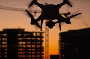 Silhouette of Unmanned Aircraft System Quadcopter Drone In The Air Over Buildings Under Construction. photo