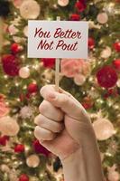 Hand Holding You Better Not Pout Card In Front of Decorated Christmas Tree. photo