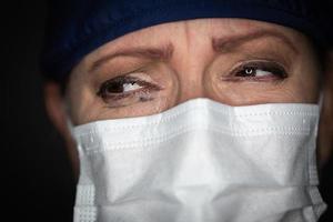 doctora o enfermera estresada y llorosa con mascarilla médica en un fondo oscuro foto