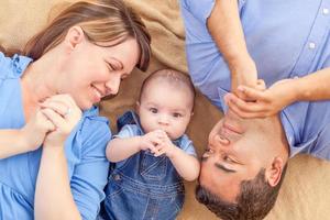 Young Mixed Race Couple Laying With Their Infant On A Blanket photo