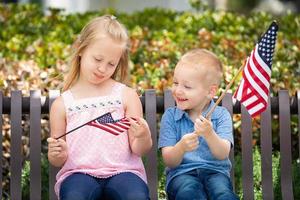 hermana y hermano jóvenes comparando el tamaño de la bandera americana en el banco del parque foto