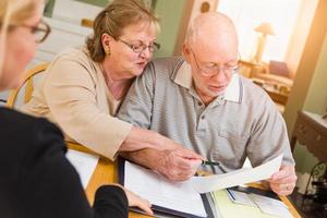 pareja de adultos mayores revisando documentos en su casa con un agente al firmar foto