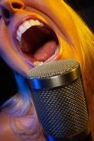Female vocalist under gelled lighting sings with passion into condenser microphone. photo